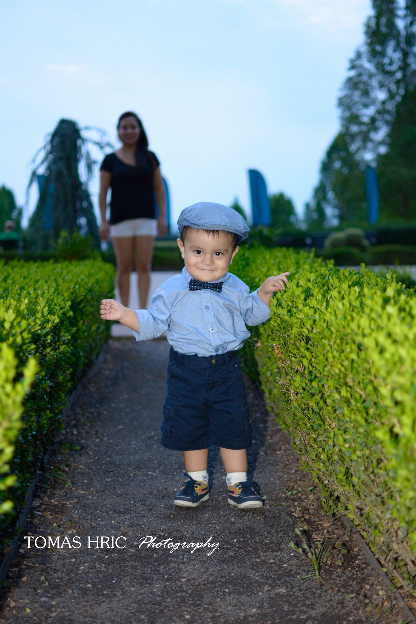 2 year old baby boy walking in th ally between bushes