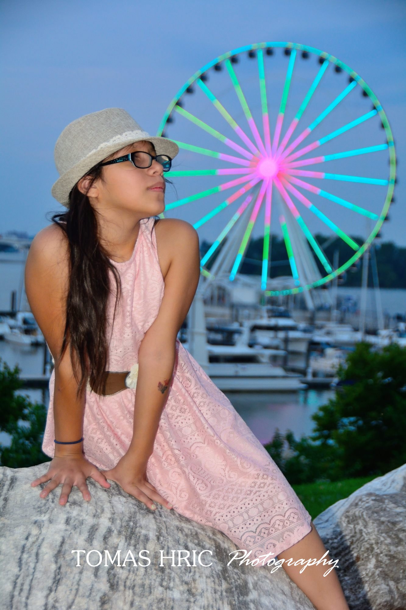 portrait of a girl with glasses on a rock in front of ferris wheel